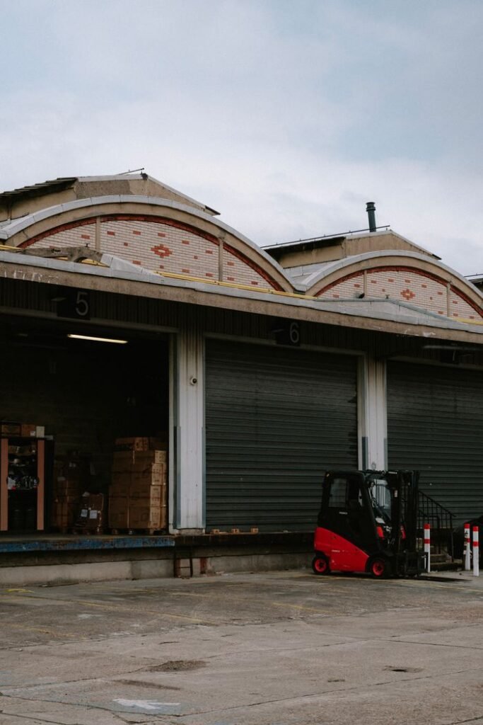 الرئيسية A red forklift parked at a warehouse loading dock with closed garage doors.